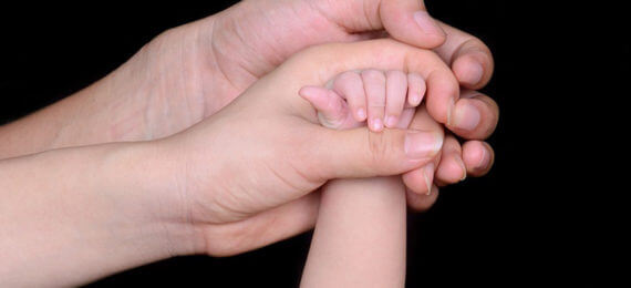 mãos do pai e mãe segurando a mão de bebê