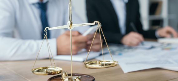 Balança da justiça com dois advogados ao fundo