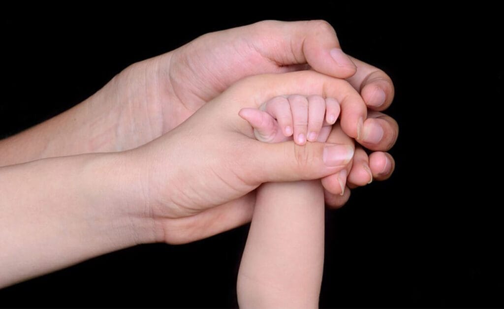 mãos do pai e mãe segurando a mão de bebê