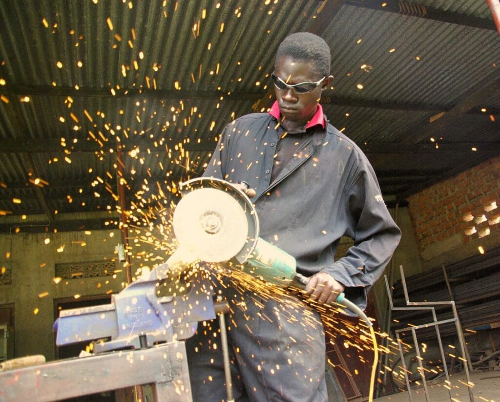 Periculosidade Insalubridade - Homem de macacão e óculos serrando uma peça de metal e produzindo faíscas