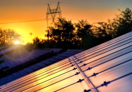 Isenção de ICMS para geração distribuída - telhados em um por do sol com um poste de rede elétrica ao fundo