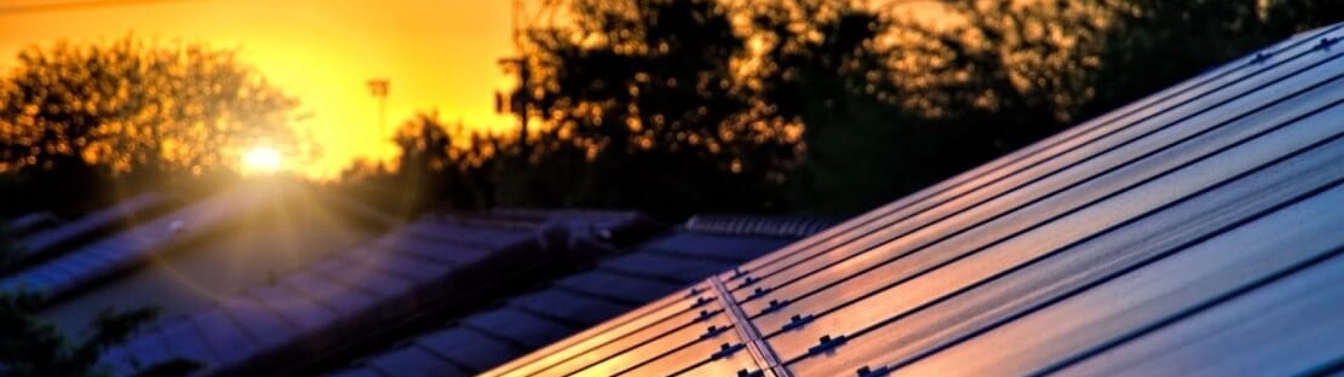 Isenção de ICMS para geração distribuída - telhados em um por do sol com um poste de rede elétrica ao fundo